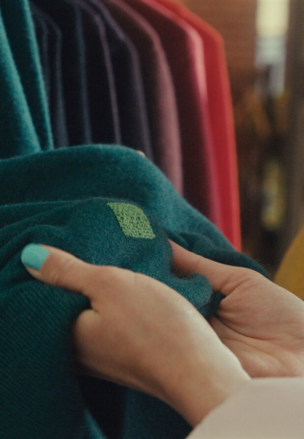 Hands showing a visible mending repair on a green sweater. 