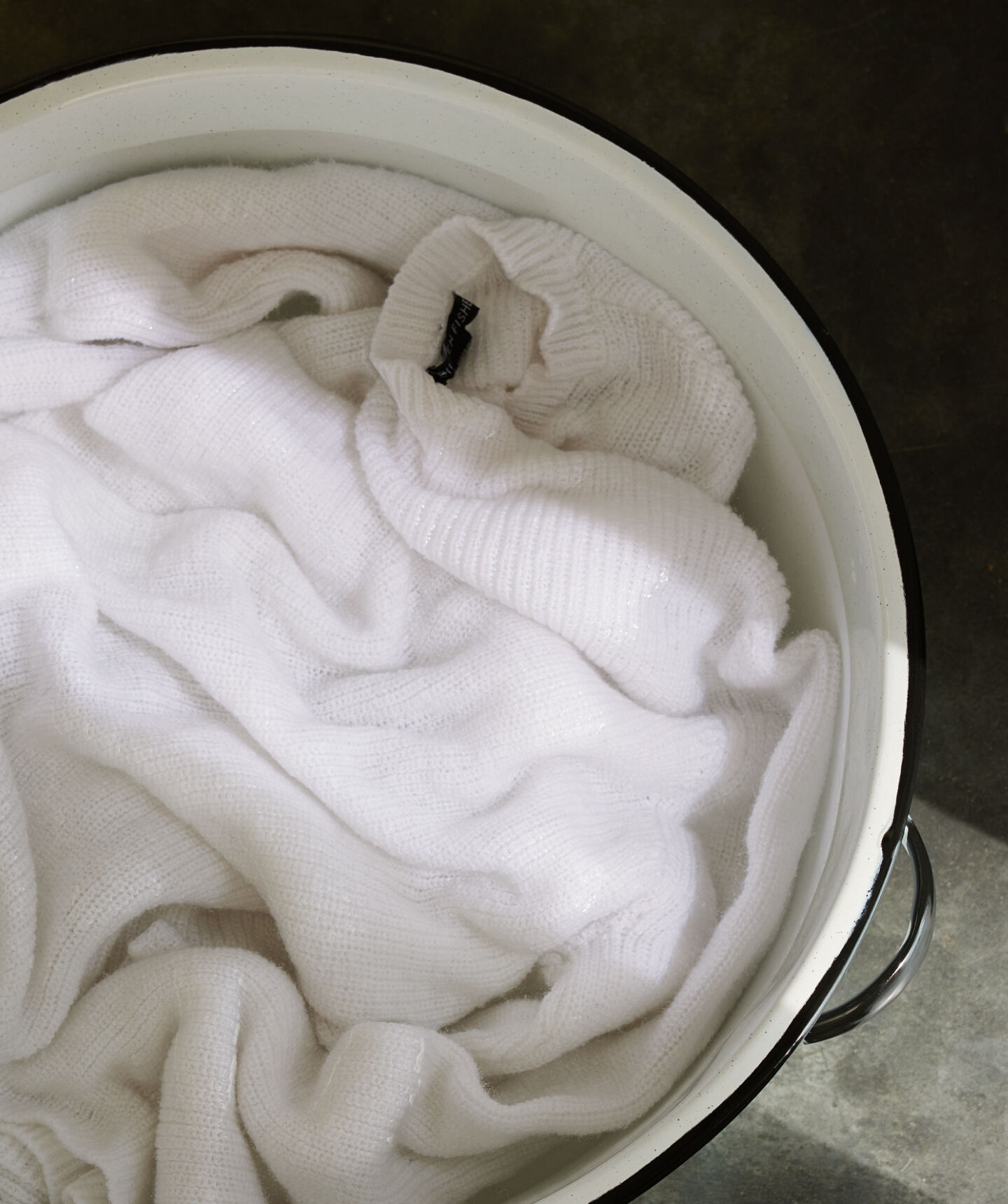 Beige sweater in basin of soapy water.