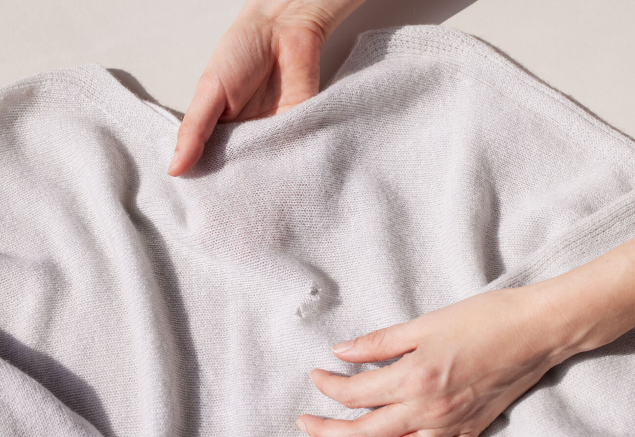 Woman's hand holding moth-eaten wool sweater.
