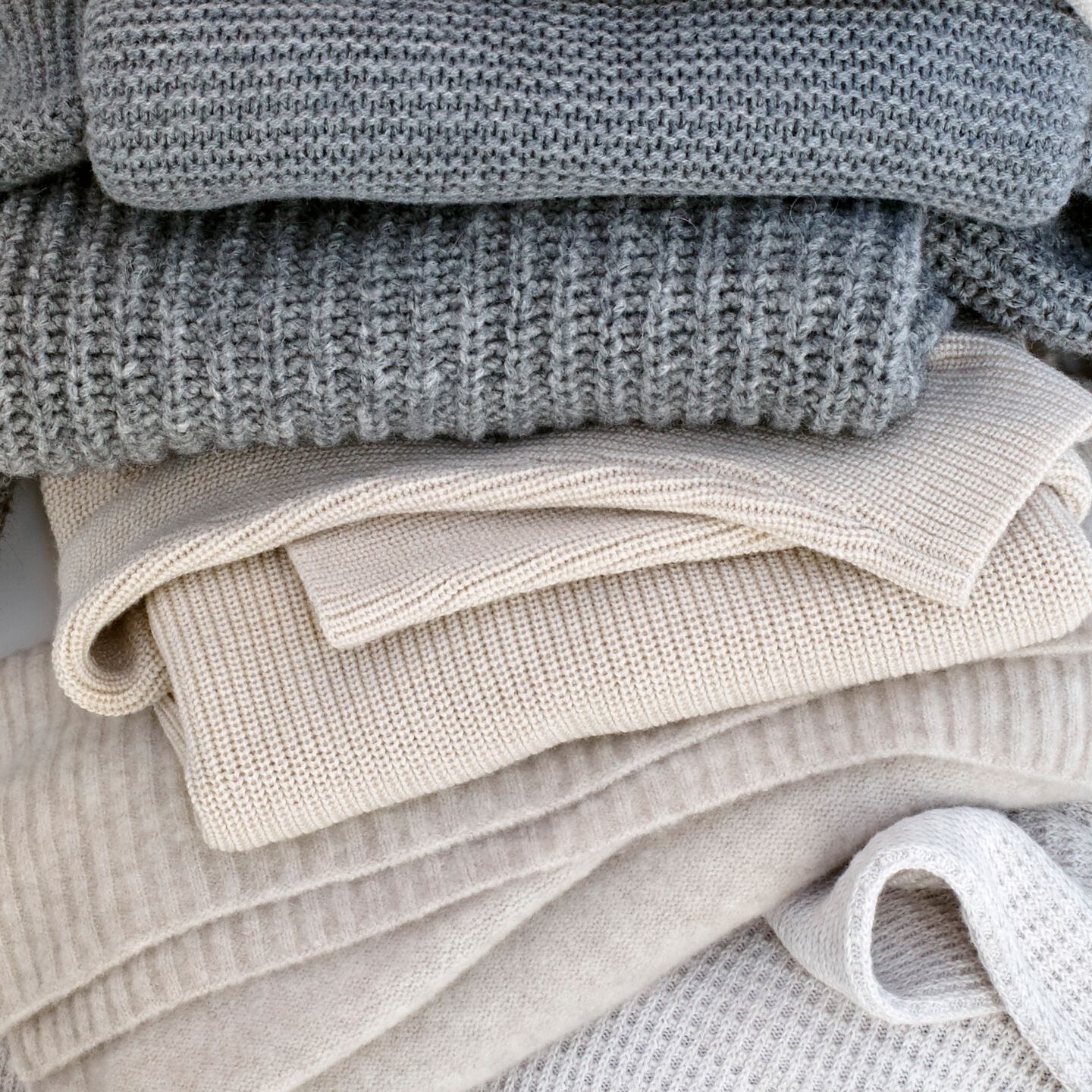 Stack of neutral sweaters and knits.