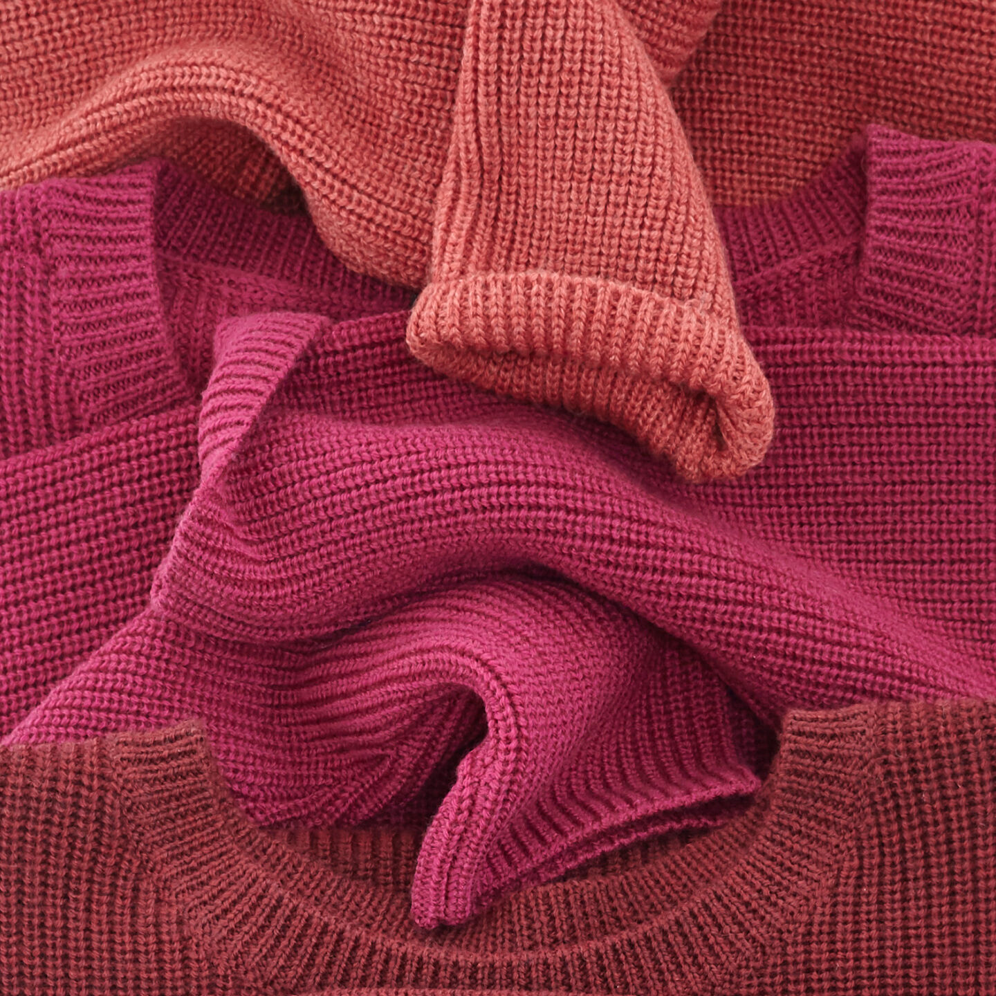 Berry colored sweaters folded in a row.