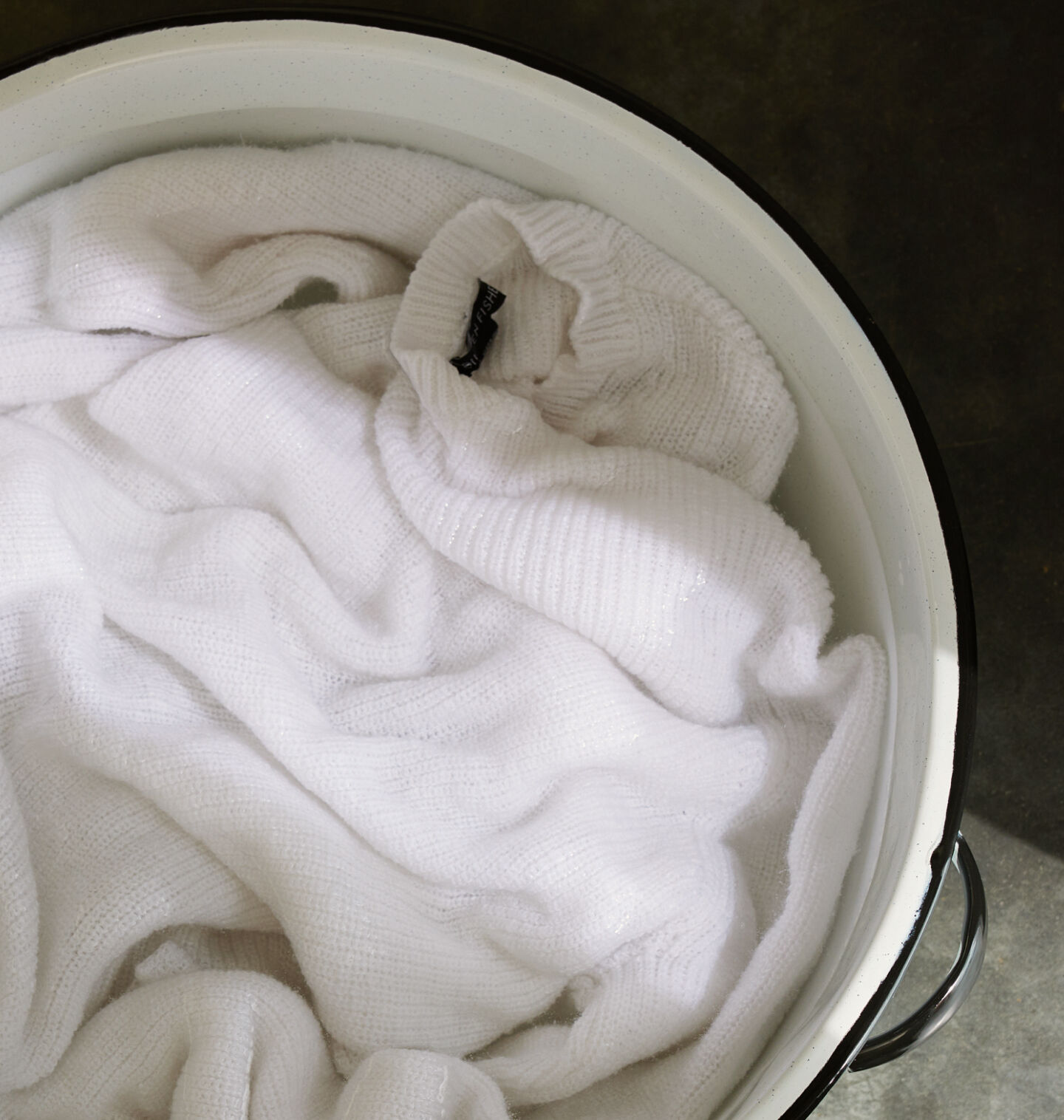 Beige sweater in basin of soapy water.