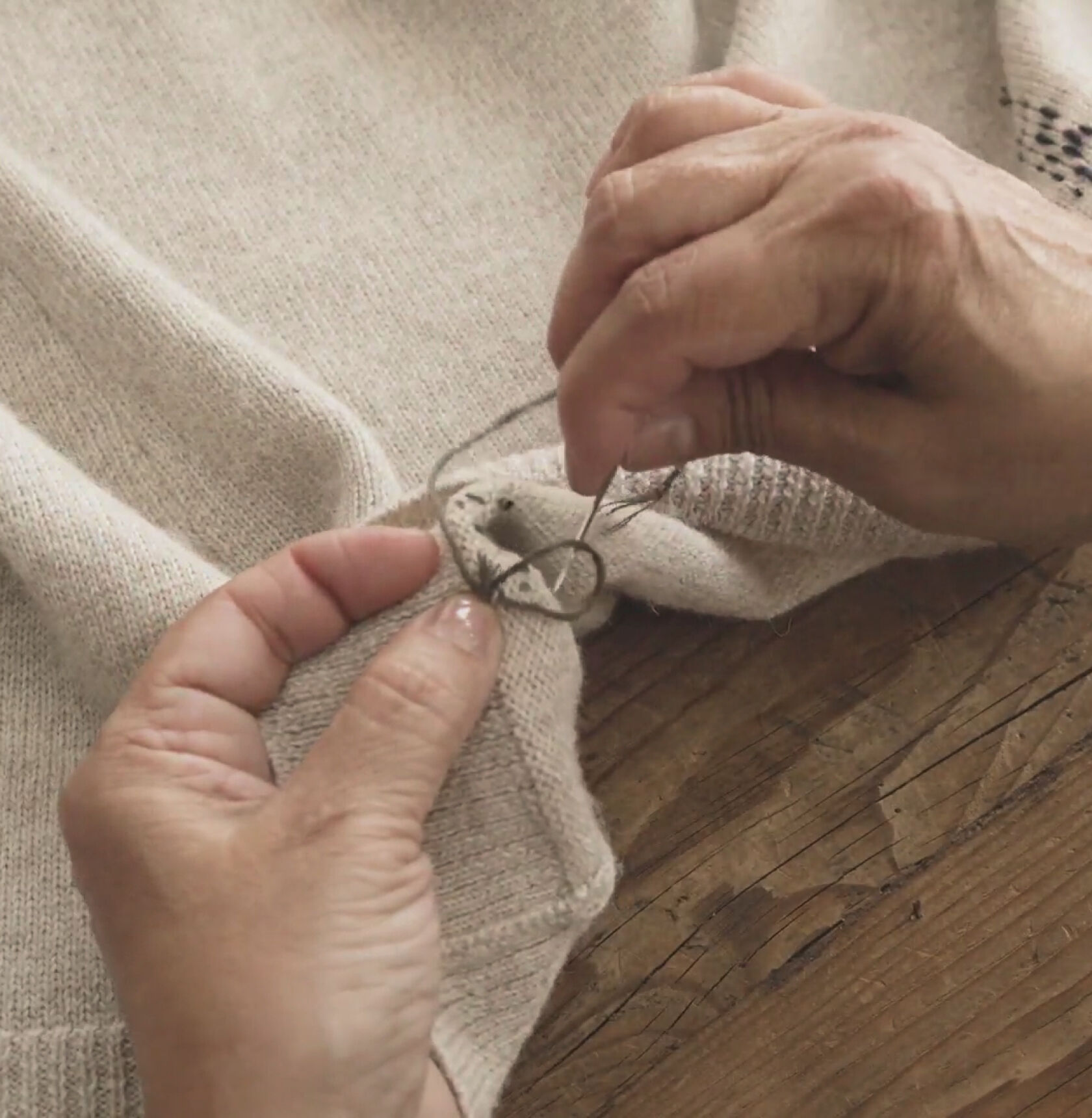 Hands knotting thread on the underside of a beige sweater.