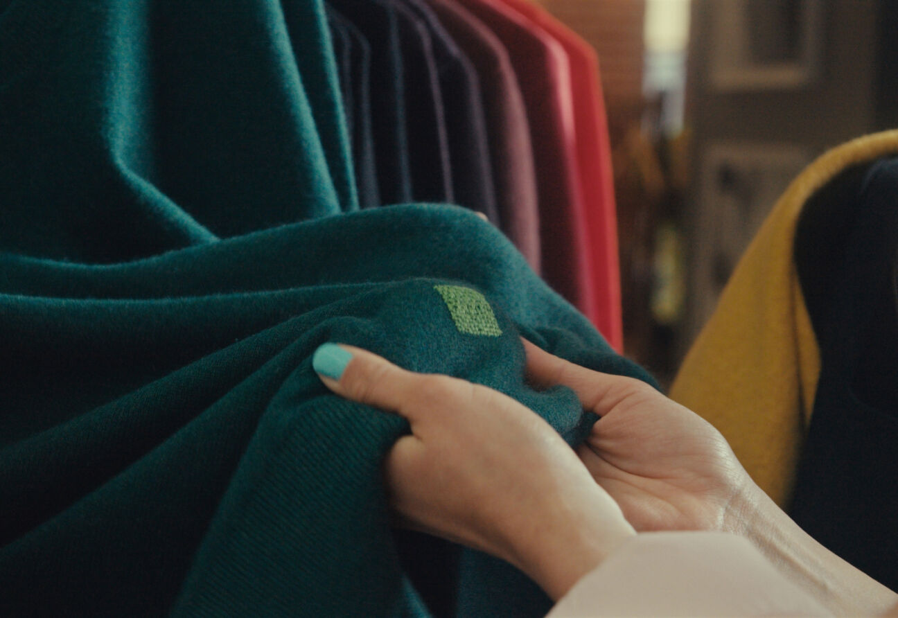 Hands showing a visible mending repair on a green sweater. 