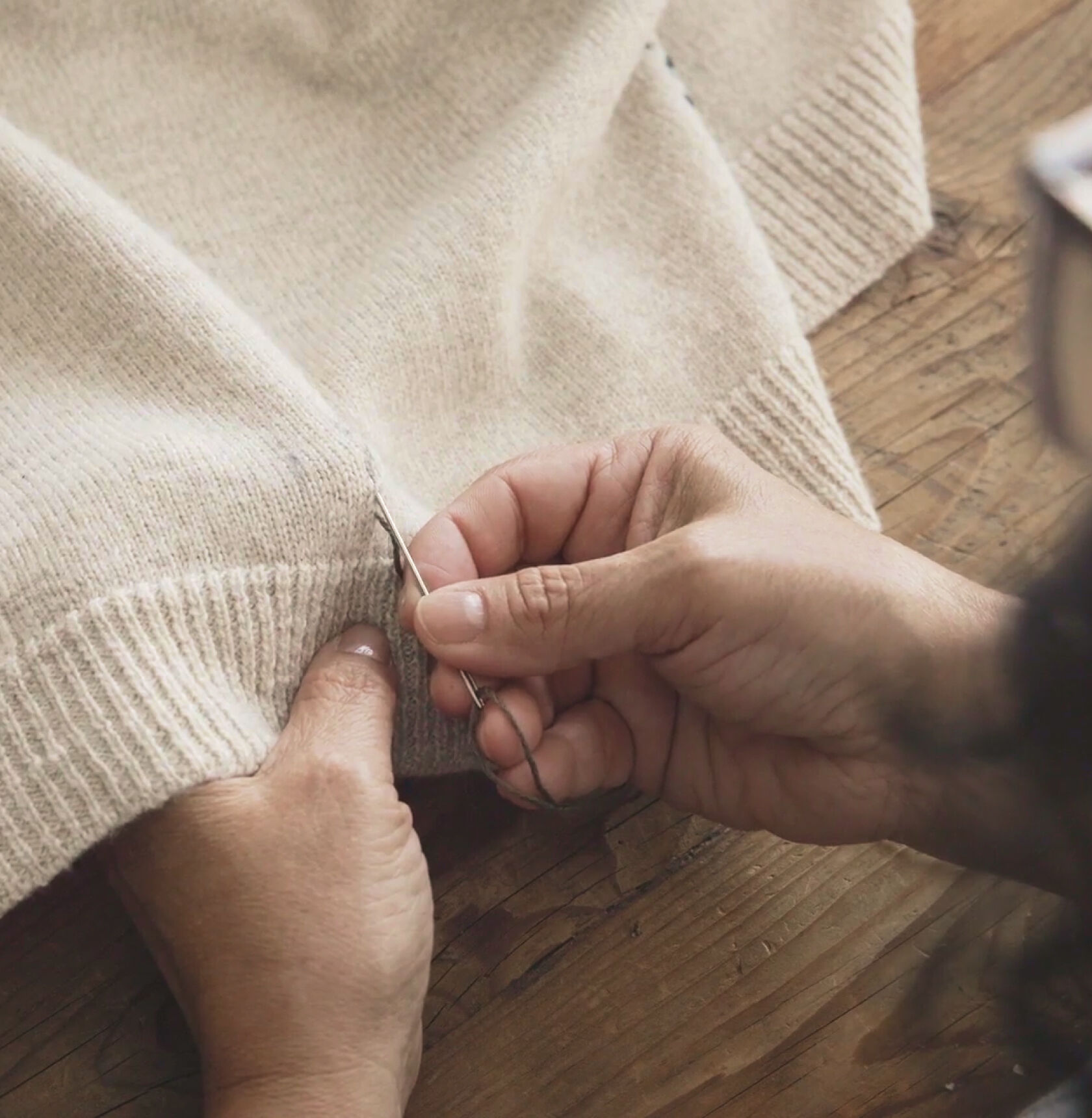 Hands doing a running stitch with a contrasting thread on a beige sweater.