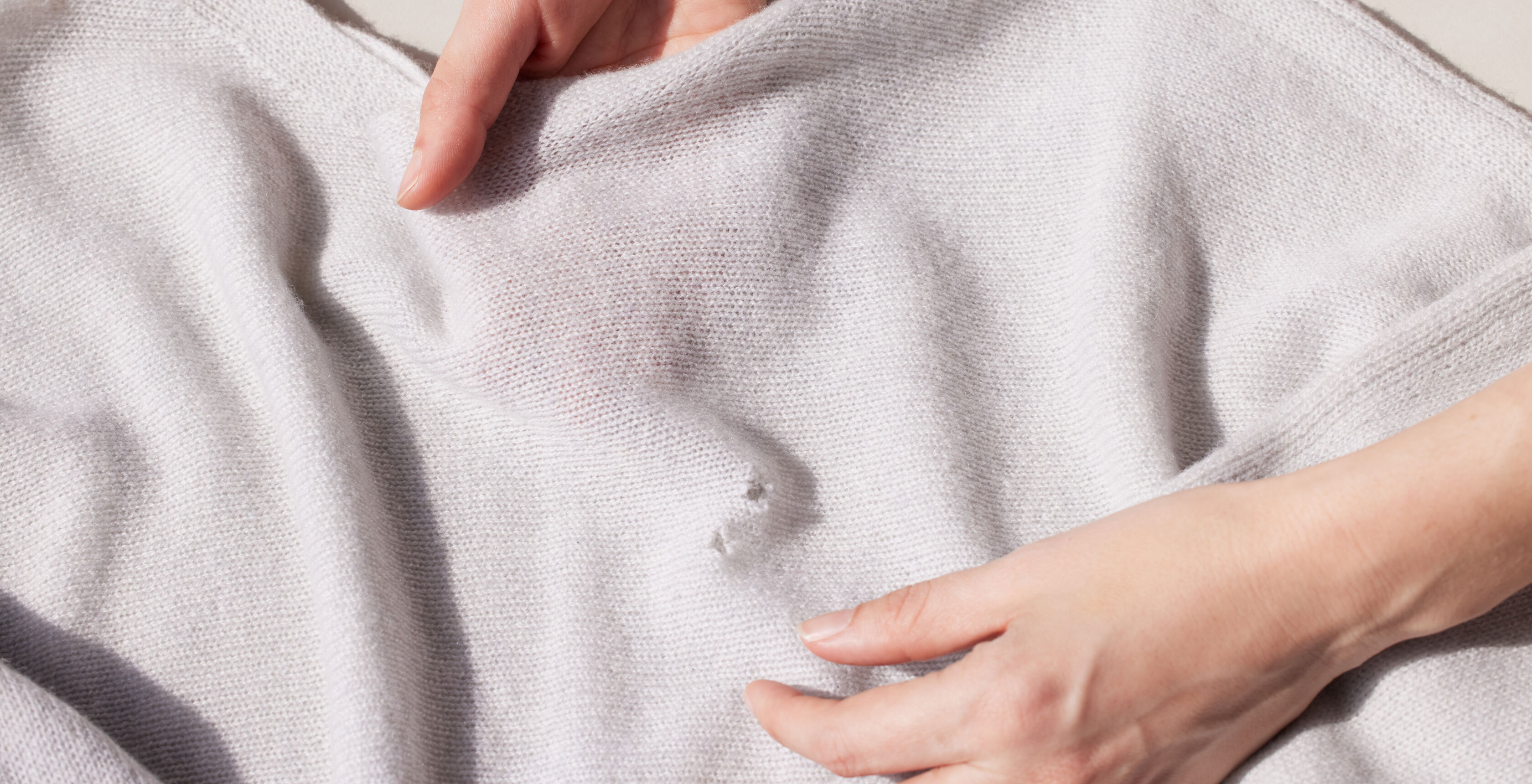 Hands holding sweater with moth holes.